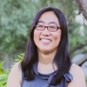 image of woman with purple shirt and medium length hair wearing glasses sitting outside smiling.