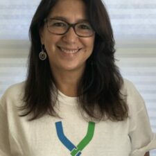 Tatiana Bejar image of Latina woman with long brown hair and glasses smiling looking at the camera wearing a white t-shirt that reads Hand in Hand: The Domestic Employers Network