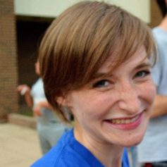 Image of white woman with head tilted smiling into camera with blue shirt.