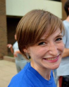 Image of white woman with head tilted smiling into camera with blue shirt.