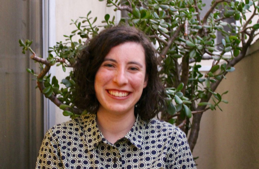 Image of white woman smiling shoulder length brown hair wearing a black and white patterned button up shirt
