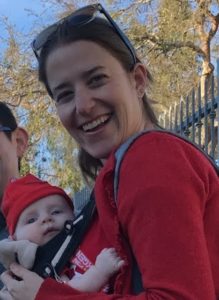 image of smiling white woman with brown hair holding a white baby in a carrier