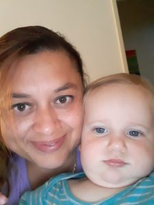 Image of woman smiling lovingly with brown hair and eyes hugging white baby