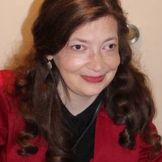 Headshot of white woman with long red hair wearing a red jacket and black shirt