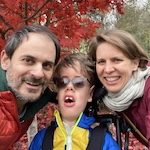 Image of a white mother and father smiling with son with a disability in a wheelchair