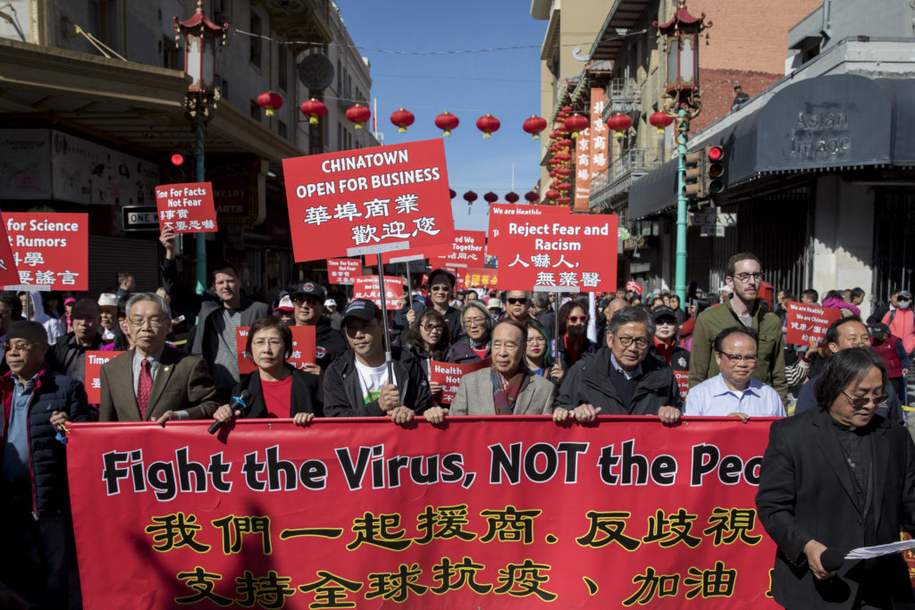 Image of Asian Americans marching with signs that say Reject Fear and Racism, Fight the virus not the people