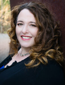 Head shot of white women with shoulder-length curly auburn hair smiling at camera