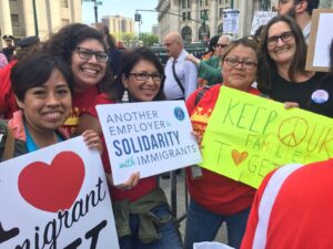 Group photo of people smiling holding signs at a rally that read "Another Employer in Solidarity with Immigrants, Keep Our Families Together