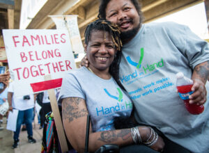 woman in wheelchair with young man hugging her and a sign with text Families Belong Together