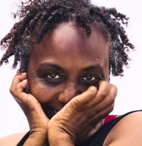 Close up head shot of black woman's face with curly hair resting head in hands