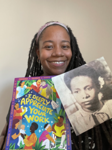 A black woman with locs smiling directly into camera against wall, holding Honor Domestic Work poster in her left hand and a black and white photo of her grandmother in her right hand. 