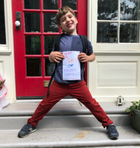 White child standing outside of house holding sign that says 1st day of Kindergarten