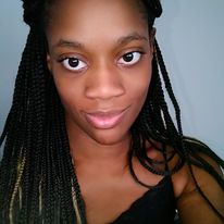 A black woman with black long braids and a black shirt smiling directly into the camera.