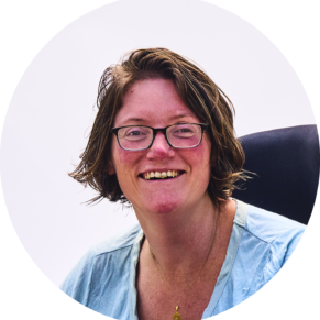 white woman with short hair and glasses wearing blue shirt smiling while sitting in wheelchair.