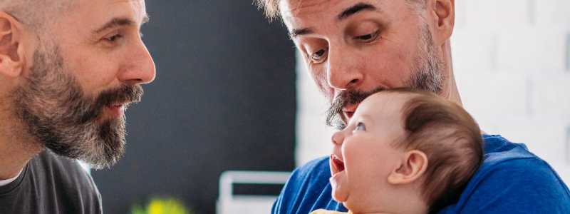 Two dads playing with their baby as the baby smiles.