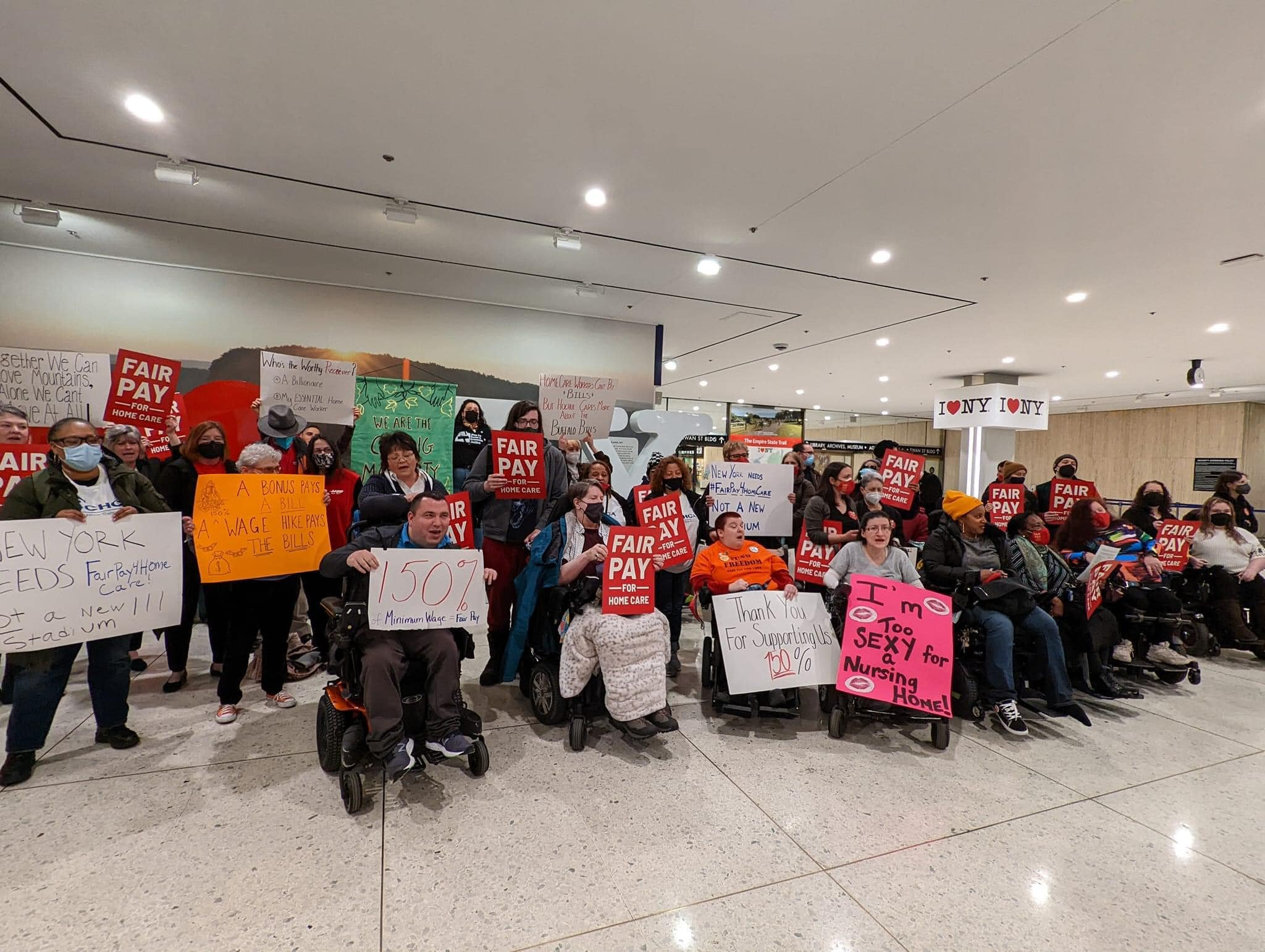 a group of people standing and sitting in wheelchair holding different posters with different phrases pertaning to Fair Pay For Home Care