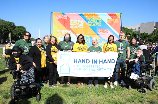 People standing and in wheelchairs wearing Hand in Hand and National Domestic Workers Alliance t-shirts, holding a banner that reads Hand in Hand: The Domestic Employers Network