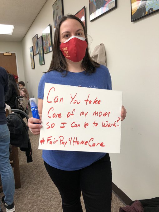 White woman wearing a mask holding a sign that reads: Can you take care of my mom so I can go to work? #FairPayForHomeCare