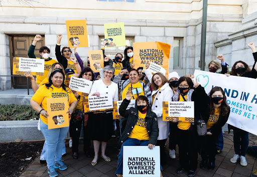 Group of people outside wearing yellow National Domestic Workers Alliance shirts while holding posters. 