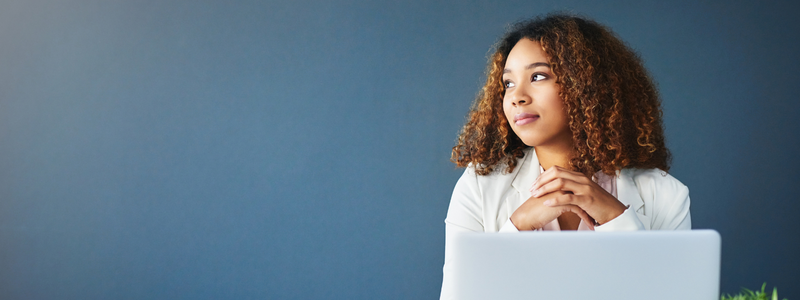 A black woman seated in front of a laptop thinking. 