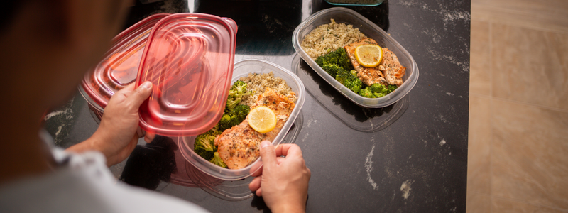 A light skinned man preparing food in containers. 