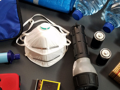 A set of emergency kit tools on a table including a mask, flashlights, water bottles, and a bag that reads "FIRST AID "