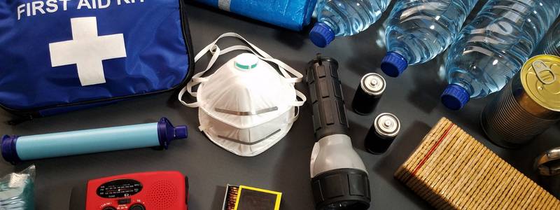 A set of emergency kit tools on a table including a mask, flashlights, water bottles, and a bag that reads "FIRST AID "