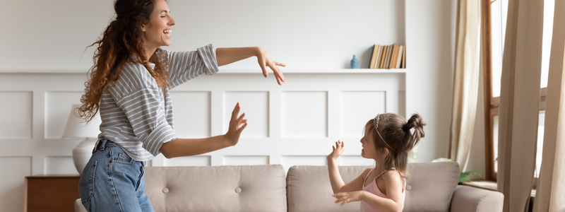 White lady with striped shirt and jeans playing with little girl in a living room. 