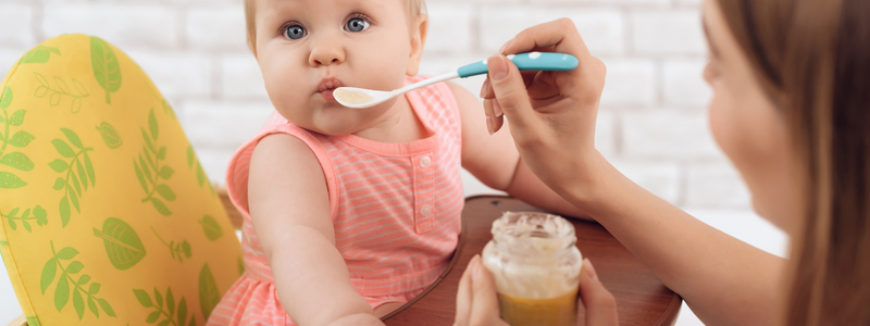 Baby being fed baby food while slightly tuning head. 