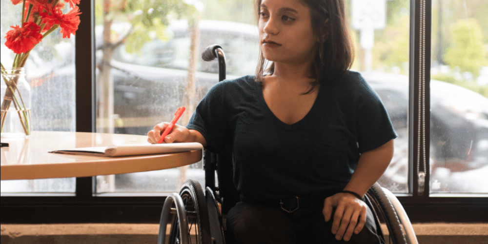 Woman in a wheelchair sitting a table holding taking notes on a pad of paper