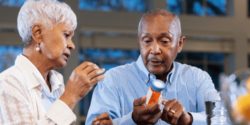 Image of older black woman sitting next to older black man who is reading a prescription bottle