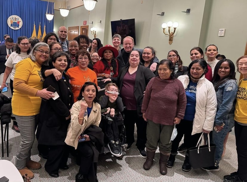 Group photo of various domestic workers and advocates of various races, ethnicities, genders and abilities, smiling and celebrating.