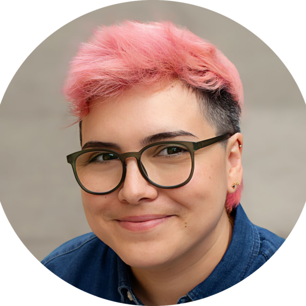 A headshot of a person with short pink hair and glasses, smiling.