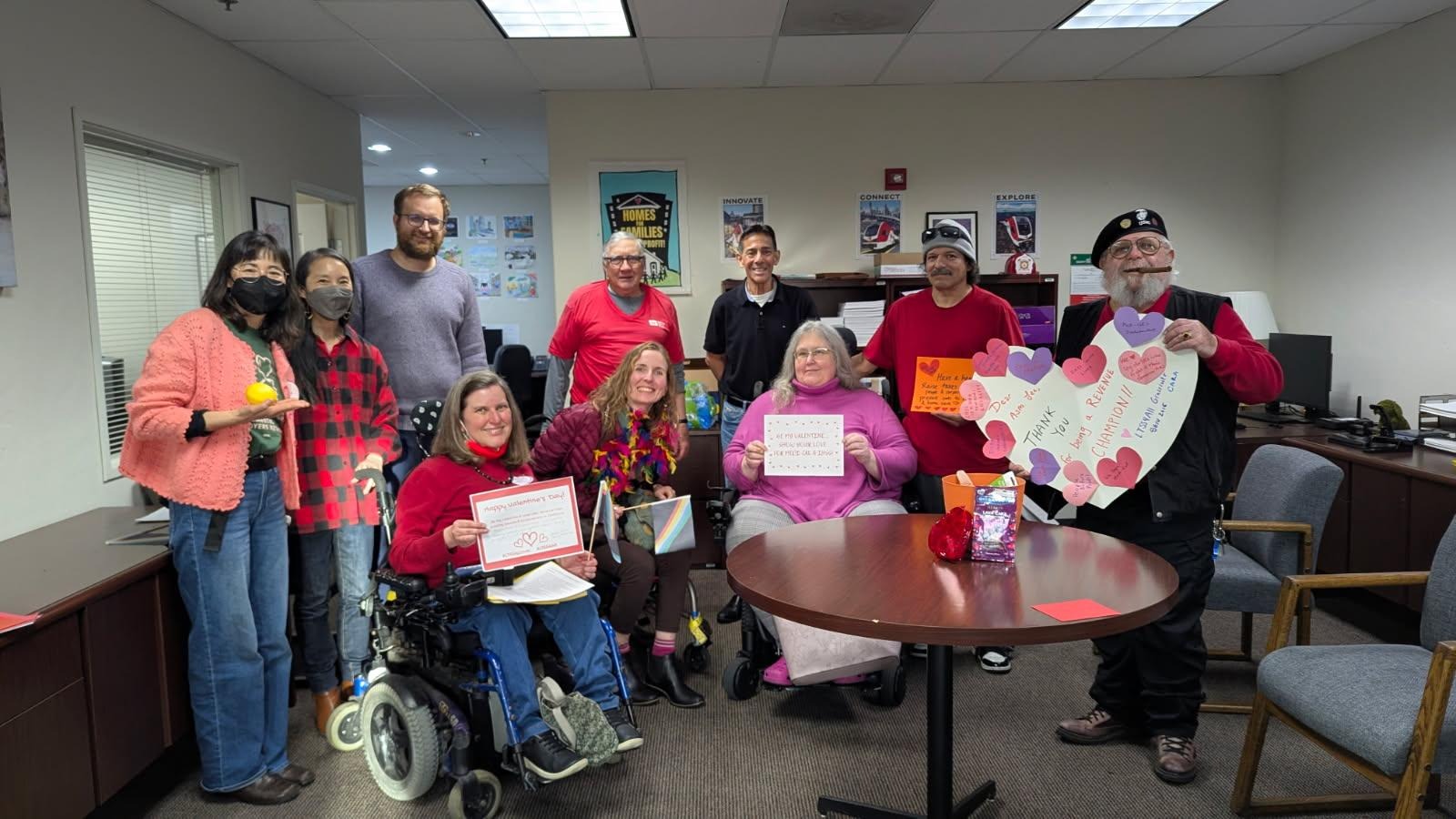 A group of people sit and stand in an office holding valentines