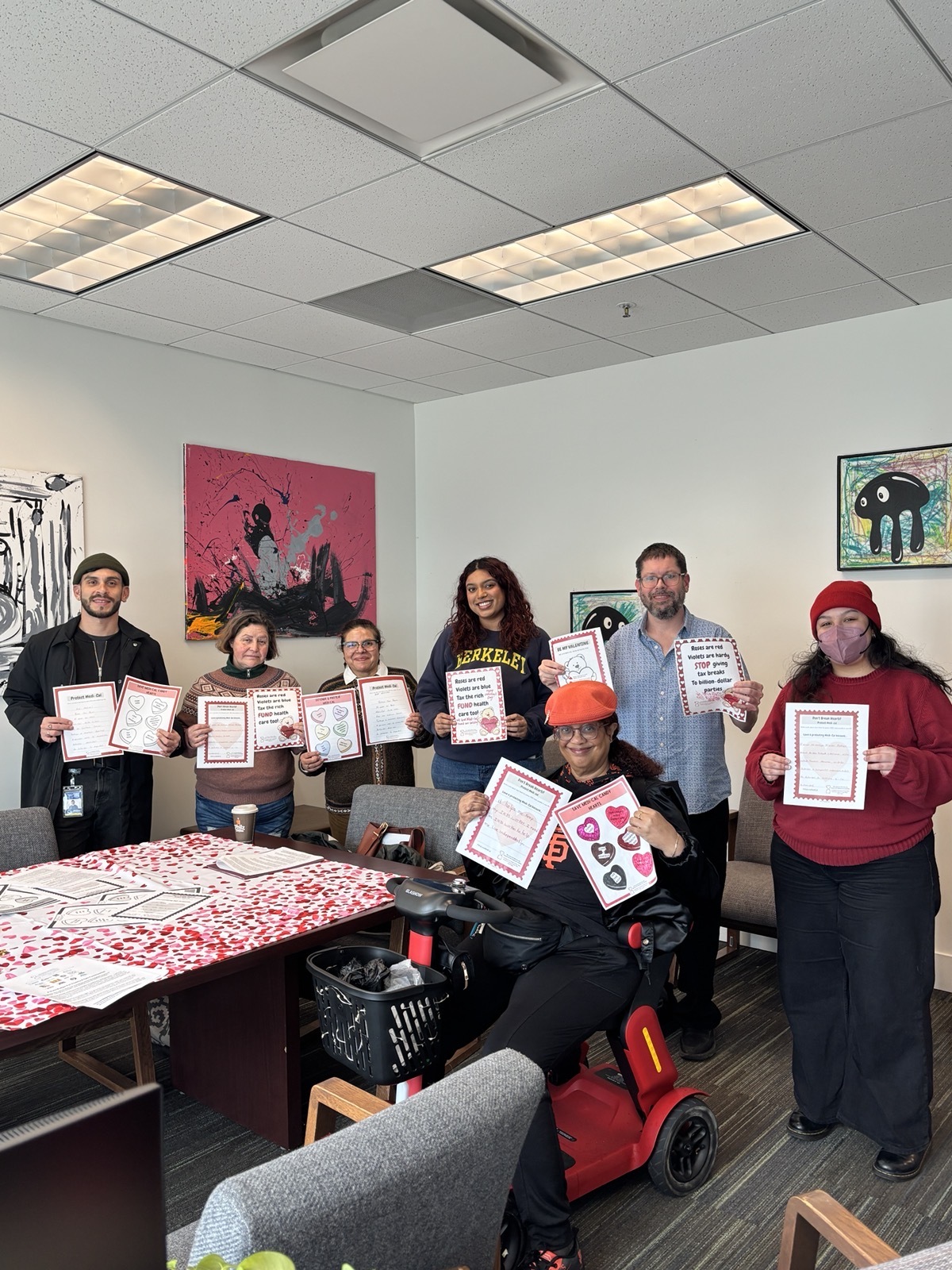 A group of people sit and stand in an office holding valentines